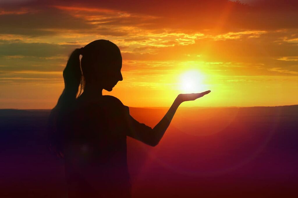 Woman looks like holding a sun on a sunset