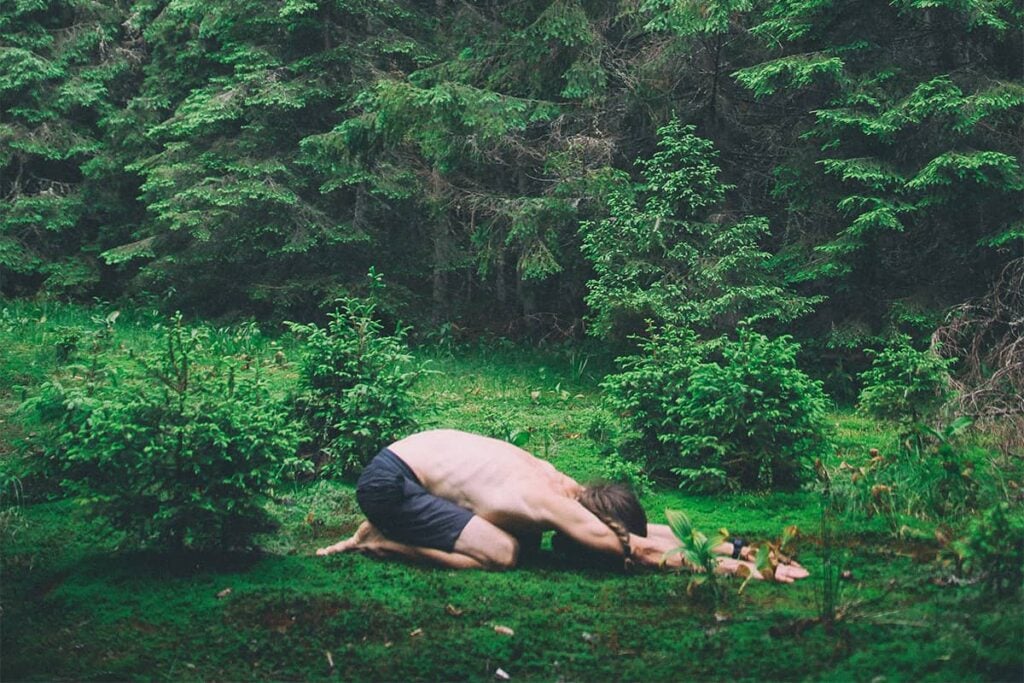Man doing child's yoga pose in woods