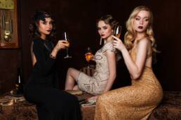 Drie vrouw in jurken die op een bank zitten met wijnglazen.