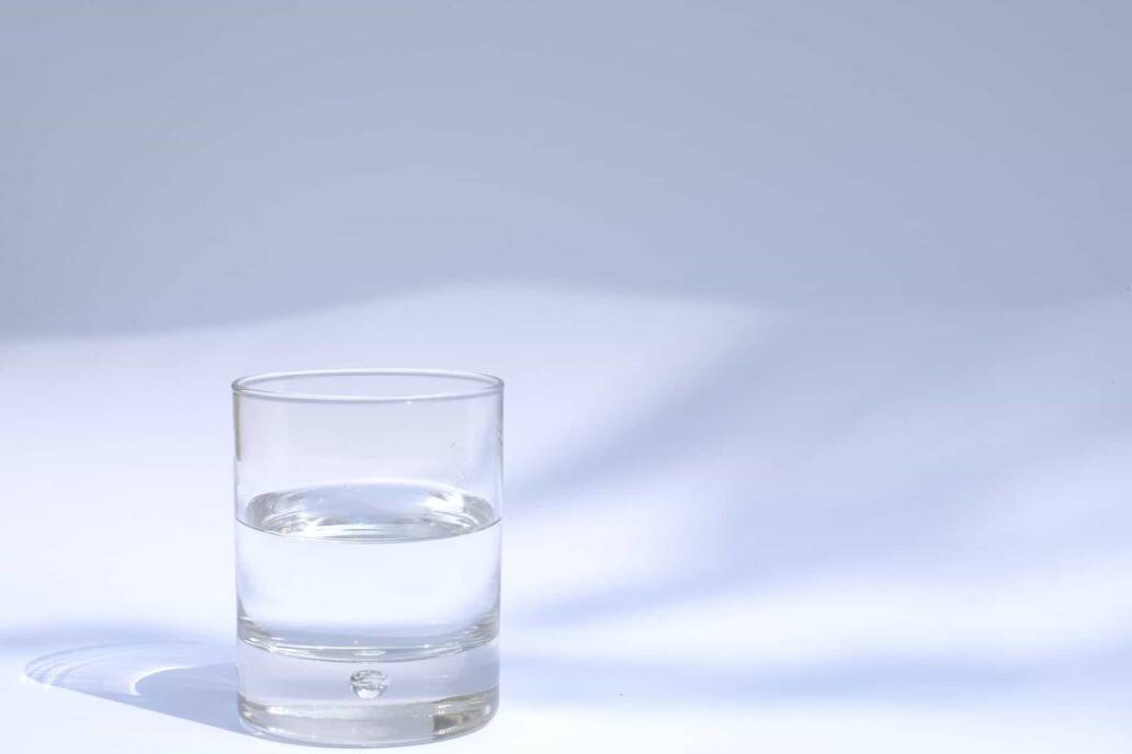 Een ontzettend glas water zit op een witte tafel met een witte achtergrond
