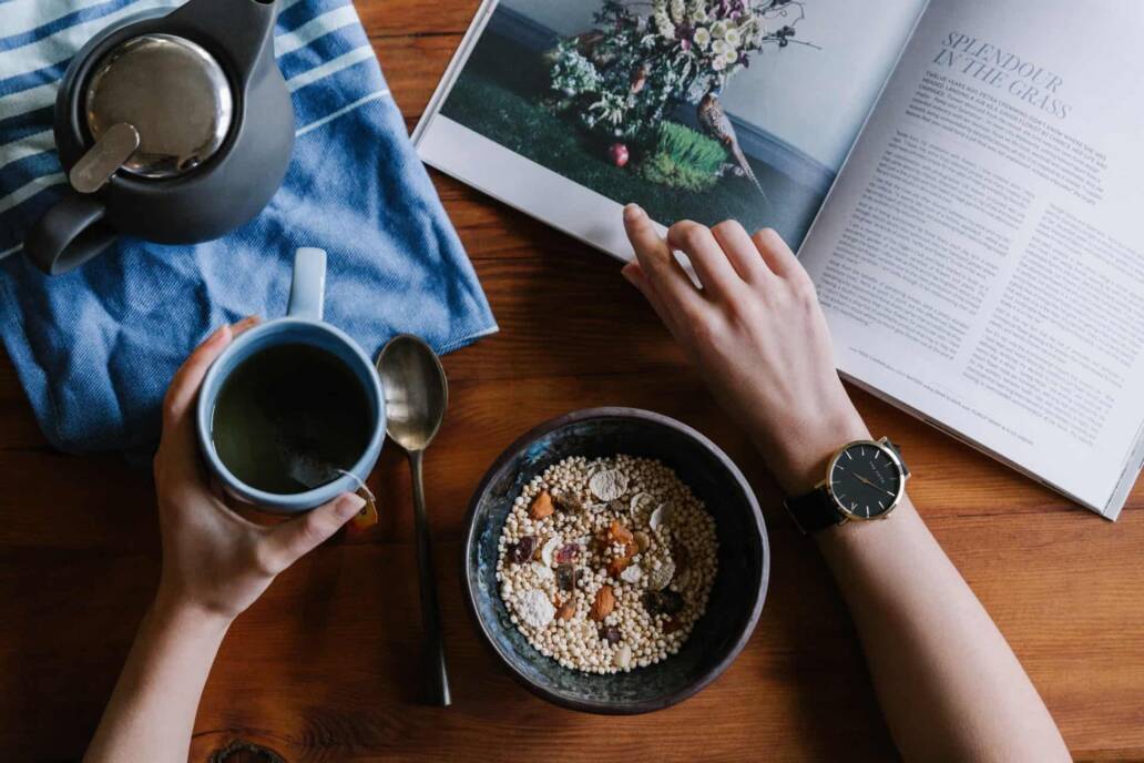 Een persoon die een tijdschrift aan tafel leest met een kopje koffie en granen